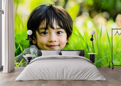 A cute Asian boy with expressive eyes lies in fresh green grass, smiling and enjoying the simplicity of nature Wall mural