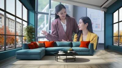 A professional photograph depicting two female entrepreneurs engaged in a collaborative discussion while diligently working in their corporate office environment. Wall mural