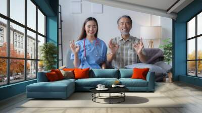 Cheerful senior man and a smiling nurse flash the okay sign, radiating positivity and trust in a cozy living room Wall mural