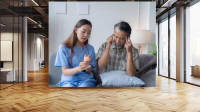 Female doctor is showing a brain model to a senior man who is touching his head, suffering from a headache, during a home visit Wall mural