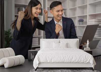 Happy young Asian businessman and woman shaking hands to congratulate successful collaboration on business deal with documents and laptop on table in the office. Wall mural