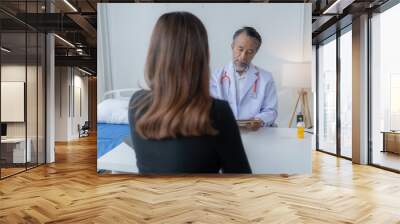 Senior male doctor is showing information on a digital tablet to a female patient during a medical consultation in a hospital room Wall mural