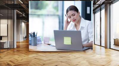 Sharing good business news. Attractive young businesswoman talking on the mobile phone and smiling while sitting at her working place in office and looking at laptop PC. Wall mural