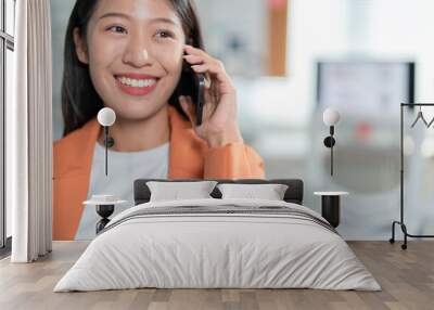 Smiling young businesswoman talks on the phone in her modern office, exuding confidence and happiness. The image captures a moment of positive communication in the corporate world Wall mural