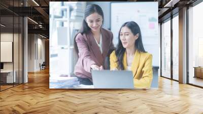 Two asian businesswomen are discussing over a laptop computer, analyzing business reports and planning business strategies for a new project Wall mural