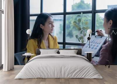 Two asian businesswomen are having a meeting in the office. They are discussing charts and graphs, analyzing financial data for their business Wall mural