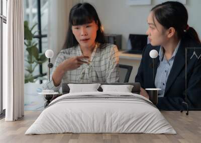 Two businesswomen are having a discussion about a financial chart, brainstorming and analyzing the company's growth and planning a business strategy for the next quarter Wall mural