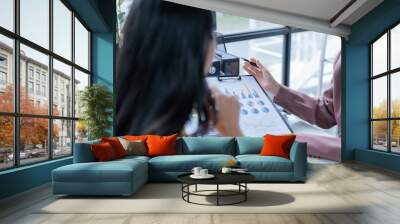 Two businesswomen discussing charts and graphs in a busy office, collaborating on strategies to boost profits using laptops and documents Wall mural