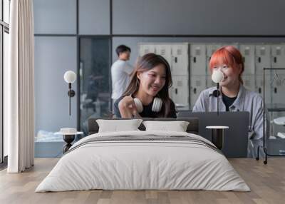 Two cheerful asian university students are working together on a project, using a laptop and sharing ideas in a modern university hallway with lockers in the background Wall mural