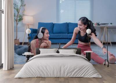 Two sporty girls wearing headphones and sportswear are stretching on a carpet at home, following instructions from an online fitness program on a laptop Wall mural