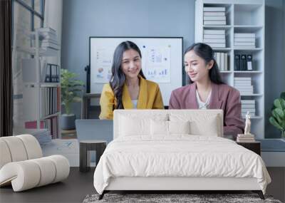 Two young businesswomen are discussing a new project, analyzing financial charts and checking data on a laptop in the office Wall mural