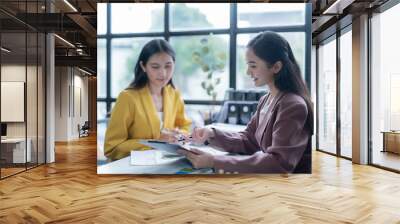 Two young businesswomen are having a productive meeting in a modern office, carefully examining financial reports and engaging in a collaborative discussion Wall mural