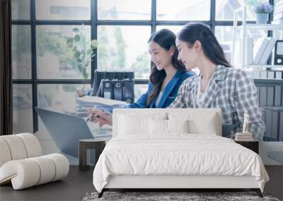 Two young businesswomen are working together in a modern office using a laptop to analyze financial data and develop a business strategy Wall mural