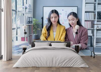 Two young businesswomen collaborate in a modern office, analyzing data and discussing financial reports. Professional and bright atmosphere with laptops and paperwork Wall mural