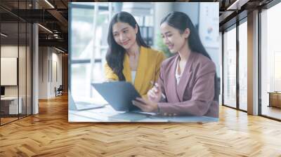 Two young businesswomen smiling, reviewing a contract in a modern office. Working together, focused on discussion, showcasing professionalism. Bright space with laptop and documents Wall mural