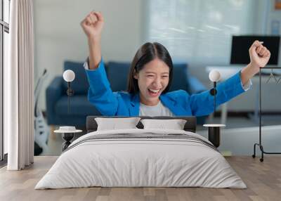 Young businesswoman is sitting at her desk with her arms raised in the air, she is happy and celebrating success in her career Wall mural