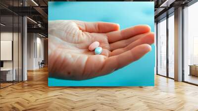 Male hand holding two pills in hand on a blue background, taking Your medication. Wall mural