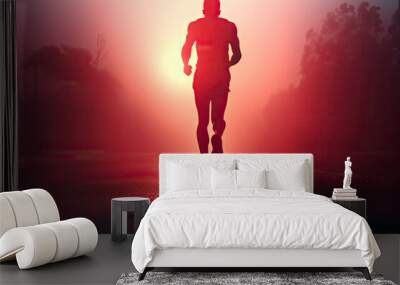 Silhouette of a jogger running along a road with the sun in his face Wall mural