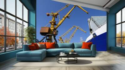 Two port cranes over an open hold. Loading a cargo ship in the port. Wall mural