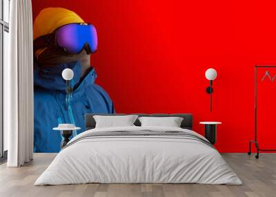 A man in spherical ski goggles looking ahead. Winter sport fashion isolated on a vivid red background with copy sapce on the right. Wall mural