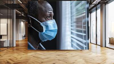 African man wearing mask, looks out during pandemic. Wall mural