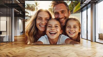 A happy family of four enjoys a sunny beach day, taking a close-up selfie with palm trees in the background and radiant smiles. Wall mural