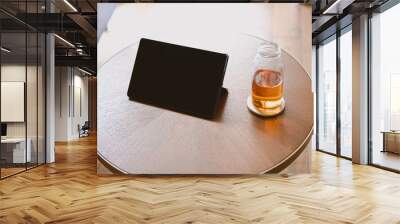 Top view of a black tablet with a blank screen on a wooden round table with a teapot o the side Wall mural