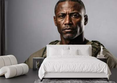 Serious black middle-aged male soldier in military gear, camouflage, intense gaze, grey background Wall mural