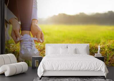 young woman runner tying her shoes preparing for a jog outside at morning Wall mural