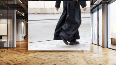 Catholic priest in the black cassock walking on the street solo, only legs visible. Clergy, faith, christianity and calling abstract concept Wall mural