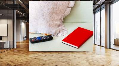 TV remote, red book and a pillow set of objects laying on an unmade bed / sofa Leisure, free time concept, staying home indoor activities, boredom, things to do Book vs tv alternative abstract, nobody Wall mural