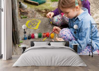 Young children painting on concrete, two girls, art, outdoor activity. Small kids spreading colorful paint on the ground using brushes, outdoors scene, closeup. Child artists, art therapy concept Wall mural