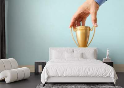 image of businessman holding a golden trophy over wooden table. Wall mural