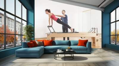 Pilates lesson on reformer, personal coaching young beautiful woman Wall mural