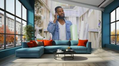 African man talking on phone pushing trolley with wallpapers in diy store Wall mural