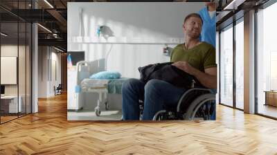 Afro female nurse talking to discharged male patient in wheelchair and smiling Wall mural