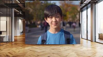 Asian schoolboy carrying backpack and smiling at camera while posing outdoors Wall mural