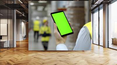 Back view of male worker in warehouse wearing safety vest standing near shelf using cellphone Wall mural