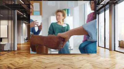 Close up of african and caucasian people holding hands sitting in circle during therapy session in support group Wall mural