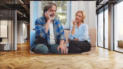 Excited senior couple receiving good news on phone talk sitting on couch at home Wall mural