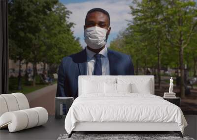 Young African businessman wearing mask for protection from corona virus outbreak walking outdoors Wall mural