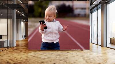 Fashionable little toddler boy with knitted outfit, walking in autumn park with phone Wall mural