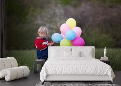 Little child, cute boy on a spring cold windy rainy day, holding colorful balloons in a field, running Wall mural