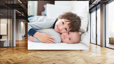 Two children, baby and his older brother in bed in the morning, playing together Wall mural