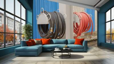 Hoses Wrapped Around Metal Stands. Two hoses, one black and one red, are neatly coiled around metal stands attached to a wall. Wall mural