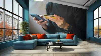 A happy young woman is shopping online via smart phone , holding credit card.. Wall mural