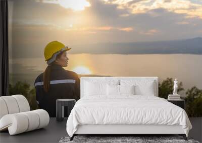 a woman engineer is putting a protective helmet on her head at sunset. Wall mural