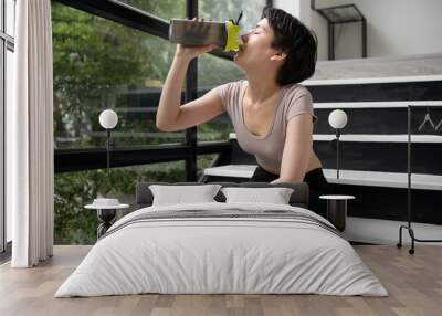 An Asian young woman is drinking protein supplements , exercise at home , healthy lifestyle concept Wall mural