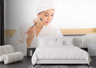 Happy beautiful woman in white bathrobe applying a face mask, skin care and treatment concept Wall mural