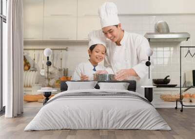 Young Asian father and his son wearing chef uniform baking together in kitchen at home Wall mural